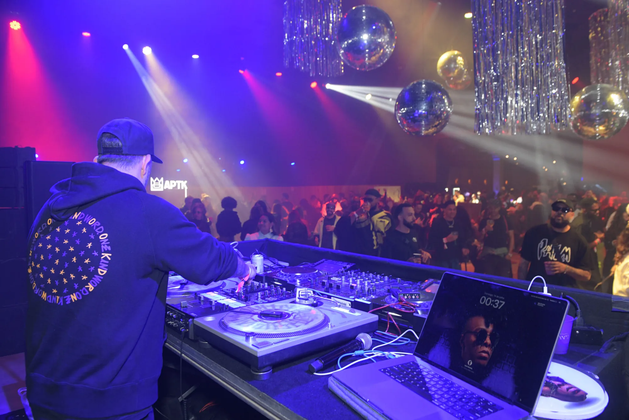 DJ toca na pista do after com globos espelhados e público ao fundo