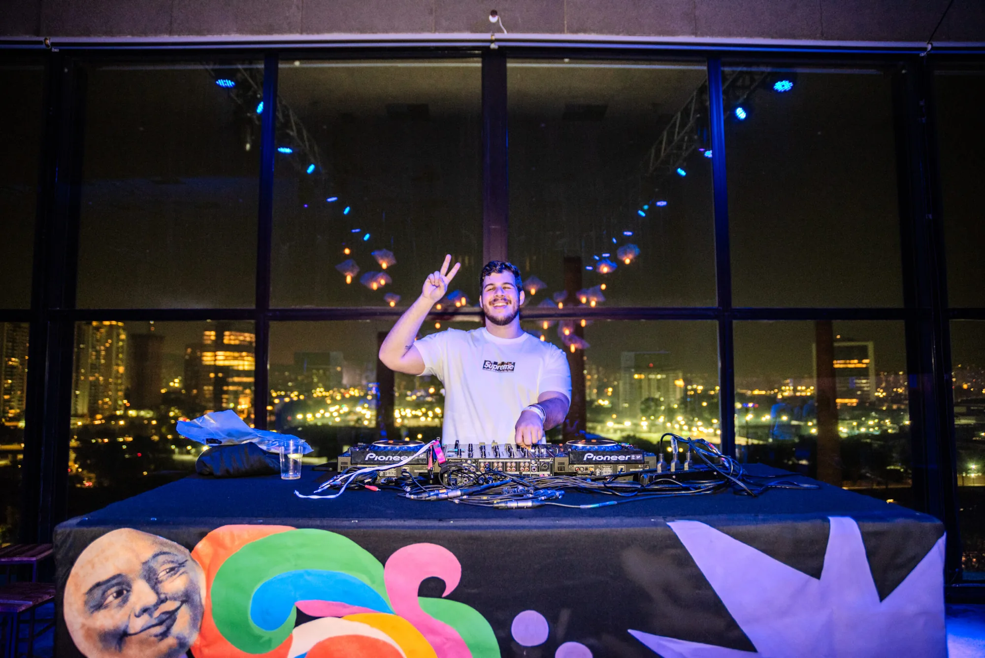 DJ toca diante do vidro com a cidade à noite